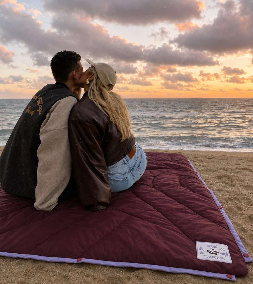 Couple on the IWANA After Hours outdoor blanket at the beach at sunset